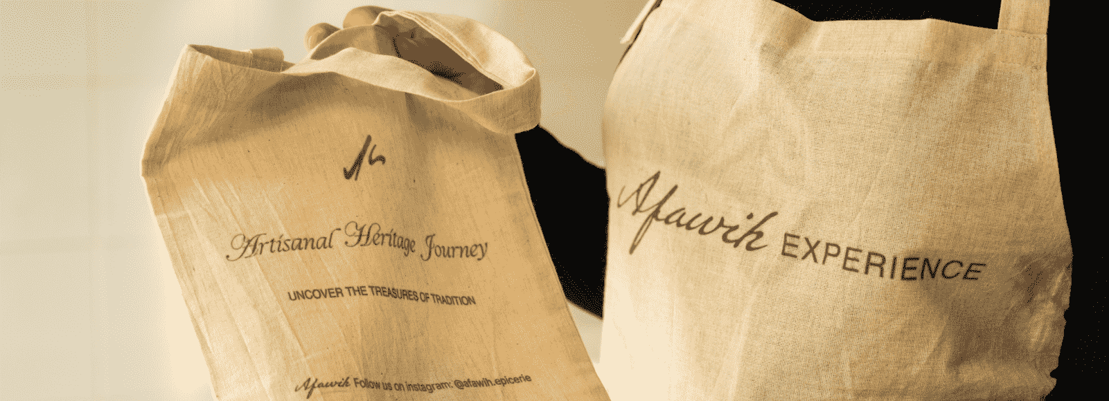 Atelier de cuisine Djeri – Une main tenant un sac en tissu beige brodé ‘Afawih Experience’, portant le logo et l’inscription ‘Ateliers de cuisine Djeri’.
